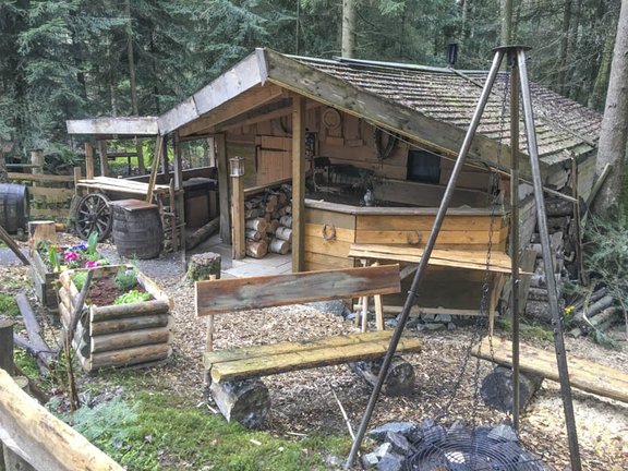 Holzhütte im Wald mit Feuerstelle und Hochbeet