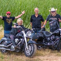 Vier Männer vor einem grünen Feld mit zwei Motorrädern