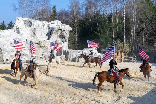 Personen reiten mit Pferden im Kreis und halten die amerikanische Flagge