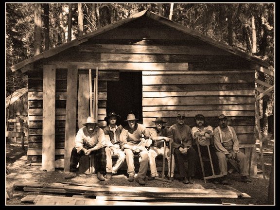 Sieben Personen sitzen vor einer Hütte aus Holzbretter