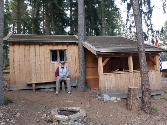 Mann sitzt auf Bank vor Holzhütte
