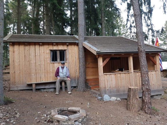 Mann sitzt auf Bank vor Holzhütte