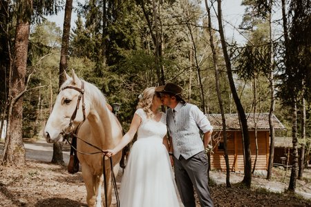 Brautpaar küsst sich. Braut hält Pferd am Zügel