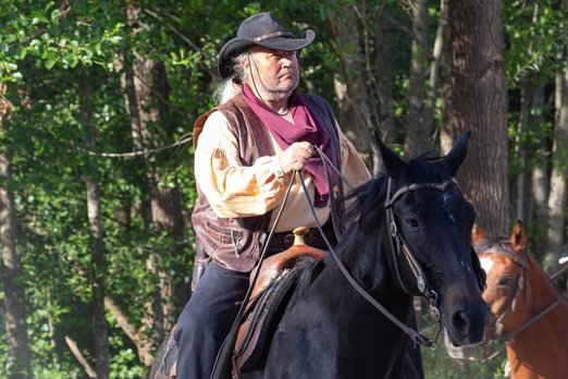 Alter Mann in Cowboykleidung sitzt auf einem Pferd