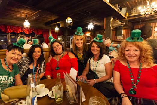 Fünf Frauen mit kleinen, grünen Koboldhüten sitzen an einem Tisch