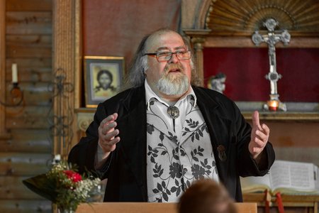 Mann mit Bart und Brille steht vor einem Altar