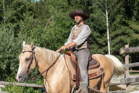 Mann in Westernkleidung reitet auf einem Pferd