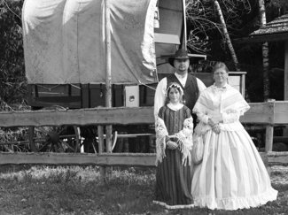 Frau, Mann und Mädchen in authentischer Kleidung aus dem 19. Jahrhundert vor einem Planwagen