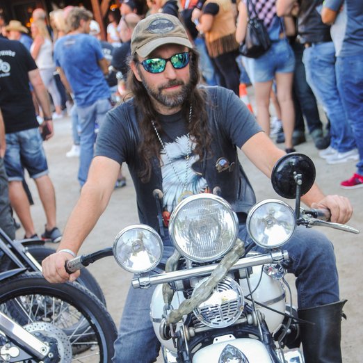 Mann mit langen Haaren, Kappe und Sonnenbrille auf einem Motorrad