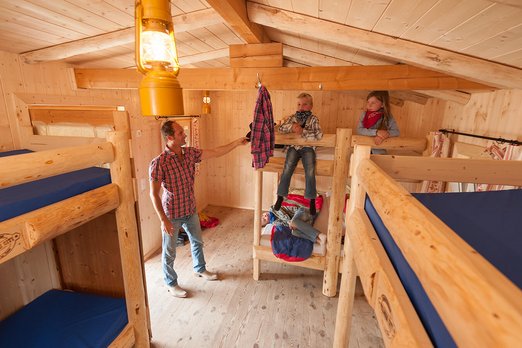 Drei Kinder sitzen auf Stockbetten, ein Erwachsener steht daneben