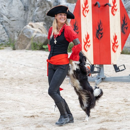 Frau in Piratenkleidung führt Trick mit Hund vor