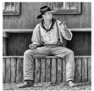 Mann in Westernkleidung sitzt auf einer niedrigen Holzwand
