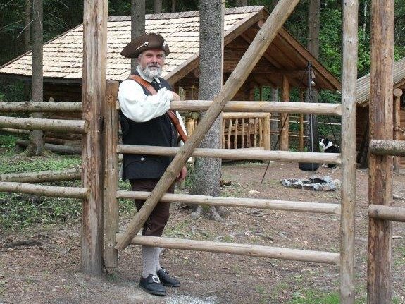 Mann in Militäruniform des 18. Jahrhunderts lehnt gegen Holzzaun