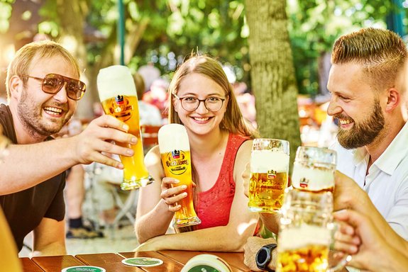 Drei Freunde sitzen im Biergarten und trinken ein Hacklberger Bier