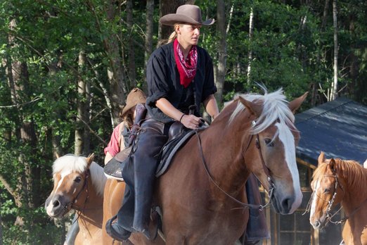 Frau sitzt in Cowboykleidung auf einem Pferd