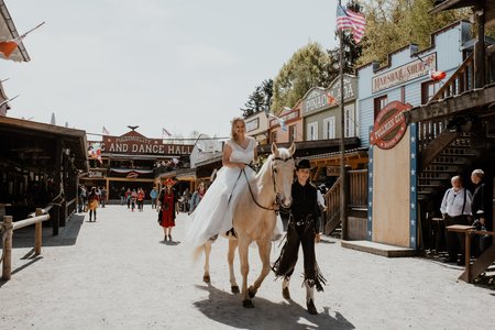 Braut reitet auf Pferd durch die Westernstadt Pullman City