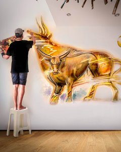 Mann steht auf einem Hocker und malt Rinder auf eine Wand