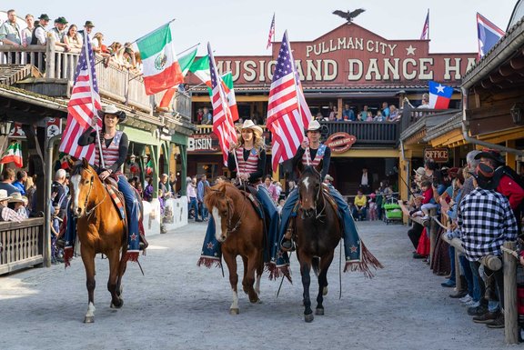Drei Reiter reiten auf ihren Pferden durch die Main Street mit amerikanischen Flaggen