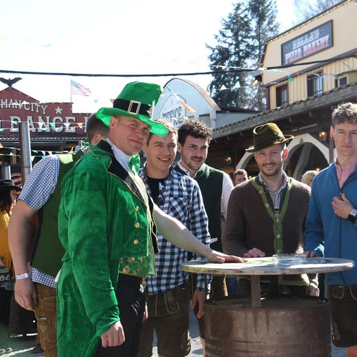 Mann in grüner Anzugjacke, Weste und Hut mit anderen Männern an einem Stehtisch