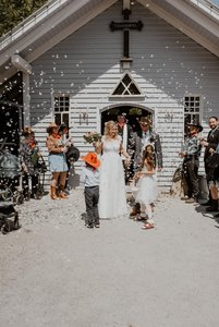 Brautpaar geht aus der Kirche heraus, Gäste werfen weißes Konfetti