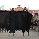 Frauen in langen dunklen Kleidern auf Stelzen
