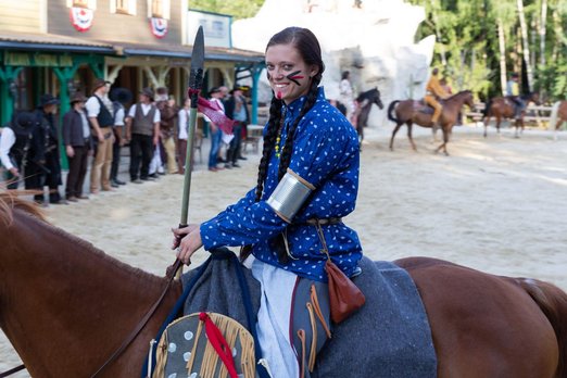 Frau mit langen Züpfen in Indianerkleidung auf einem Pferd