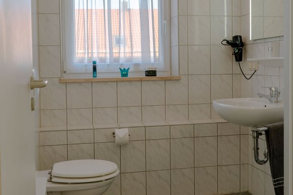 Badezimmer mit Toilette, Waschbecken, Spiegel und Föhn