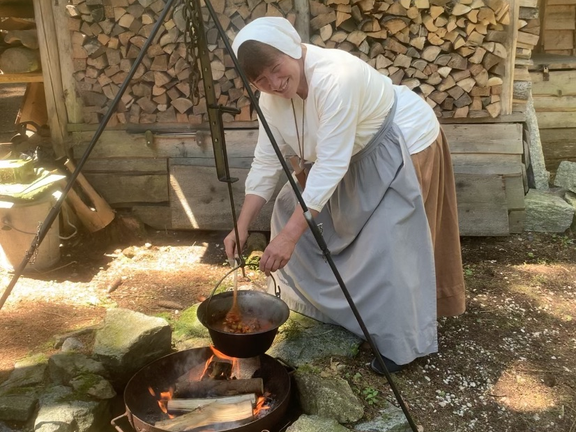 Frau in einfacher Kleidung kocht über Lagerfeuer