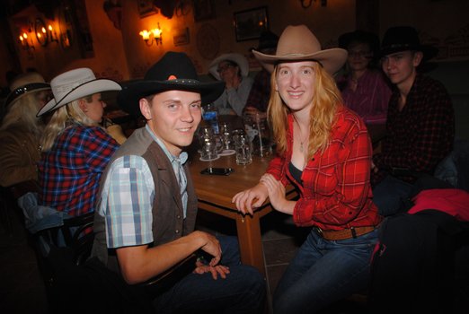 Zwei Personen in Westernkleidung am einem Tisch mit Menschen